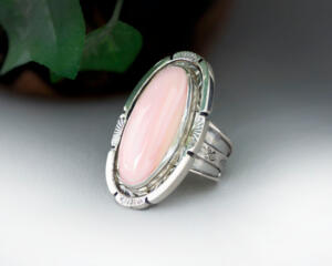 large oval pink conch stone bezel set accented with stamped cutout wire on tapered wide band